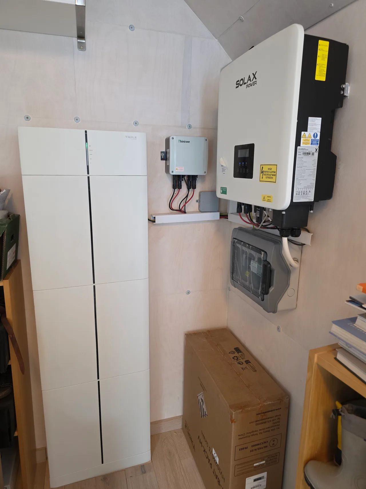 Falra szerelt SolaX Power inverter és elosztódoboz, mellette a magas, fehér Triple Power akkumulátor-torony.