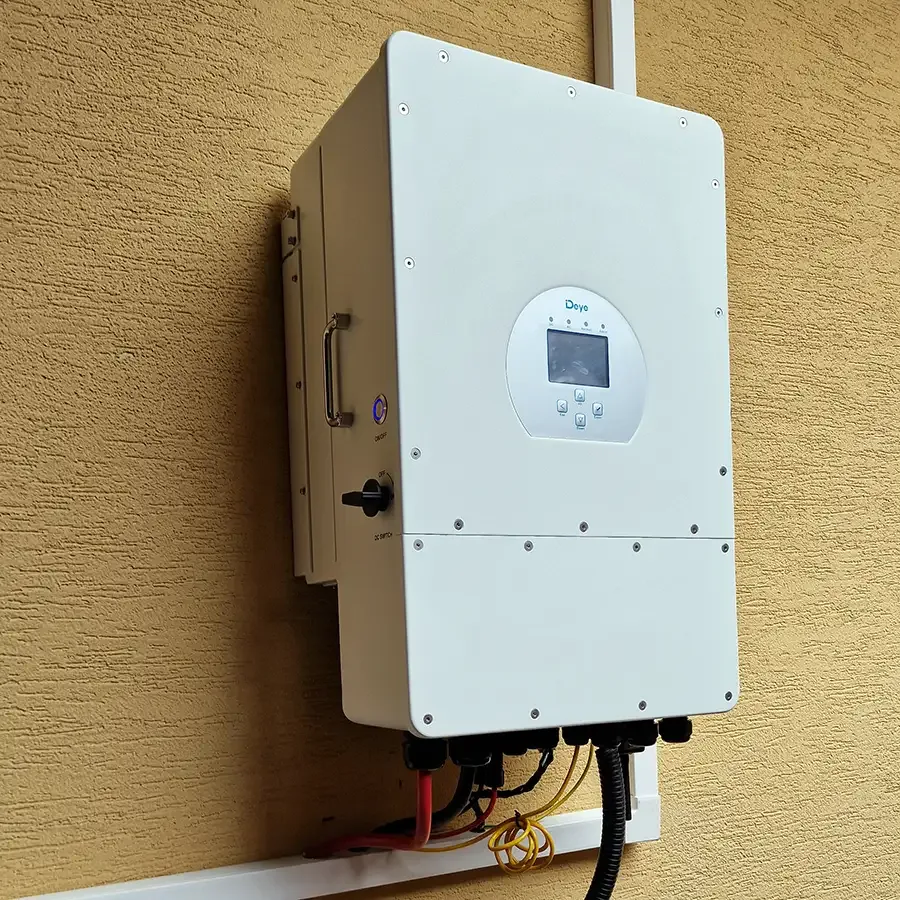 Falra szerelt Deye hibrid inverter sárga homlokzaton, alatta a bekötött kábelek.